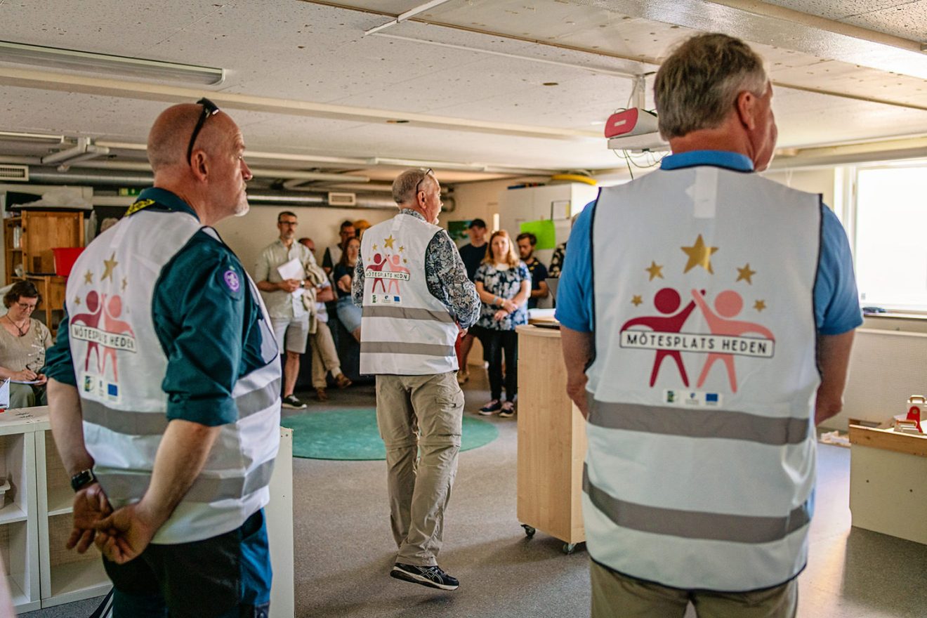 Människor med logga för Mötesplats Heden på sina ryggar, inomhus