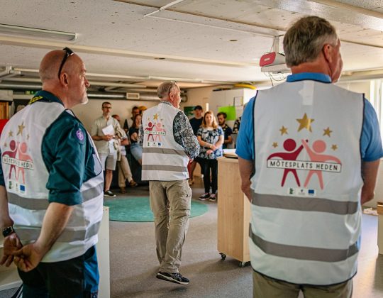 Människor med logga för Mötesplats Heden på sina ryggar, inomhus