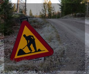 Bild på grusväg i gles skog, i förgrunden vägarebetesskylt